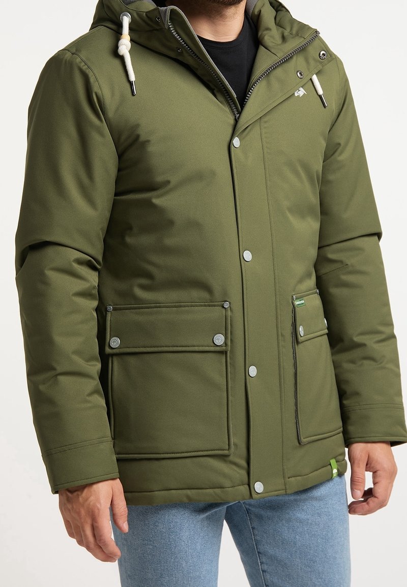 Olivgrüne isolierte Jacke mit Kapuze, Druckknöpfen auf der Vorderseite, zwei Seitentaschen und einem kleinen grünen Akzentanhänger. Glatte Stofffläche.