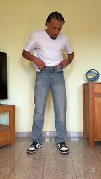 Jeans de ganga azul clara com um corte reto, combinados com uma t-shirt branca de mangas curtas e ténis pretos com detalhes brancos.