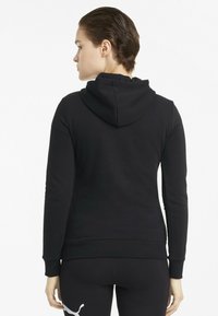 Felpa nera con un tessuto testurizzato, con cappuccio e polsini a coste, indossata con leggings neri. Design semplice, senza loghi visibili o motivi.