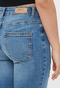 High-waisted, light blue denim jeans with a slightly faded finish and a small leather patch labeled "ONLY." Features two back pockets.