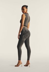 Harmaat farkut korkealla vyötäröllä, tiukalla leikkauksella ja takataskuilla, yhdistettynä yhteensopivaan hihattomaan crop-toppiin. Läpinäkyvät korkokengät.