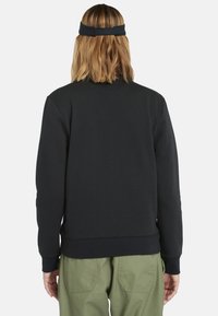 Felpa nera con scollo rotondo e maniche lunghe, realizzata in tessuto morbido. Presenta polsini e orlo a costine, abbinata a pantaloni cargo verde oliva.