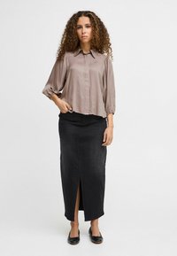 Braune Seidenbluse mit Kragen und gerafften Ärmeln, kombiniert mit einem schwarzen Denim-Maxirock mit Schlitz vorne und flachen schwarzen Schuhen.