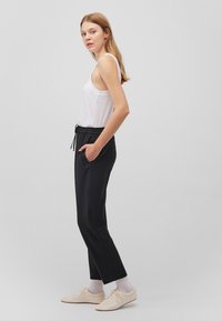 Black jogger pants with elastic waistband and side pockets, paired with a fitted white tank top. The model wears light beige shoes and socks.