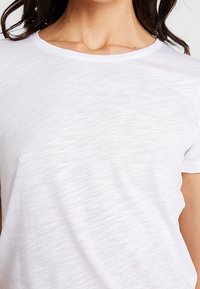 Bílý krátký rukáv tričko s kulatým výstřihem, s jemně texturovanou tkaninou a uvolněným střihem.