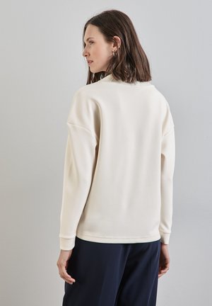 Krämfärgad sweatshirt med rund halsringning, sänkta axlar och ribbade ärmslut. Slät textur, enkel design och avslappnad passform.