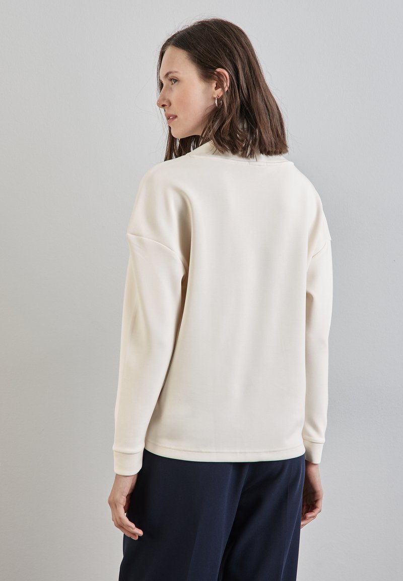 Cream-colored sweatshirt with a round neckline, dropped shoulders, and ribbed cuffs. Smooth texture, simple design, and relaxed fit.