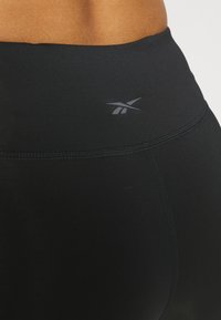 Svarta högmidjade leggings gjorda av stretchigt tyg med en mjuk textur och subtil sömnad, med en liten grå logotyp på midjebandet.