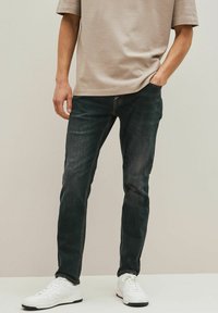 Mørke denimjeans med slim fit, prydet med subtile falmninger og syninger, parret med en beige kortærmet skjorte og hvide sneakers.