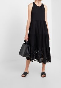 Černé bezramínkové šaty s vrstvovým designem, se vyšívaným lemem. Slučují se s černou taškou a sandály na klínku. Hladká textilie.