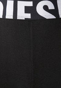 Black leggings with a thick elastic waistband featuring bold white letters. The fabric is smooth, indicating stretch and comfort.