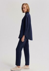 Conjunto de camisa y pantalones de color azul marino en una tela suave, con un ajuste relajado, puños abotonados y deportivas blancas. Diseño simple y limpio.