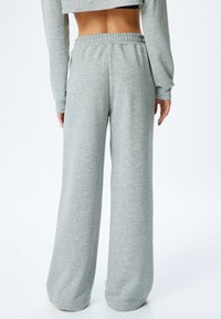 Grijze sweatpants met een relaxte pasvorm, elastische tailleband en een soepele textuur, met een iets gecropte top die van achteren is te zien.