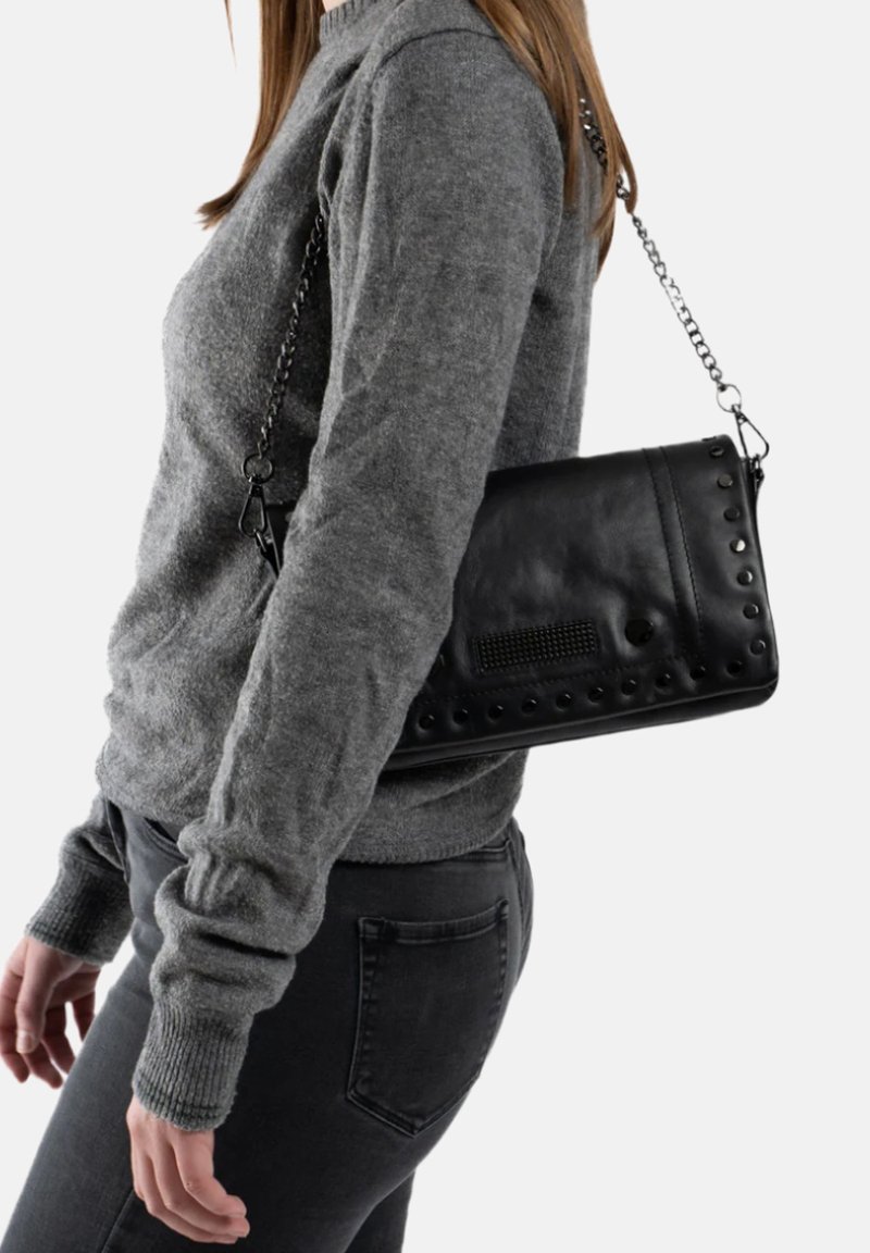 Zwarte leren schoudertas met gestikte accenten en een textuurpaneel, voorzien van een kettinghengsel. Draagt over een grijze trui en zwarte jeans.