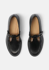 Scarpe in pelle nera con design a T e fibbia in argento, con una texture liscia e dettagli di cucitura sul bordo. Forma classica arrotondata.