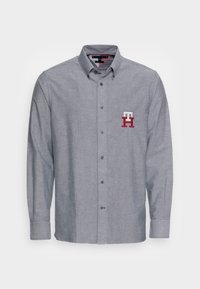 Grå långärmad skjorta med knapp fram, med krage och broderad röd och vit logotyp på bröstet samt matchande fickflik. 