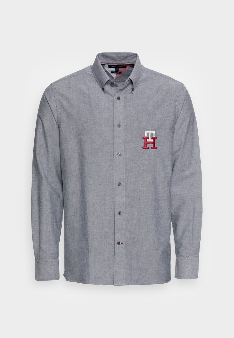 Grå långärmad skjorta med knapp fram, med krage och broderad röd och vit logotyp på bröstet samt matchande fickflik. 