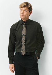Ciemnozielona, wzorzysta koszula z długim rękawem, w zestawieniu z kwiatowym krawatem w odcieniach brązu. Czarne spodnie i pasek dopełniają outfit.