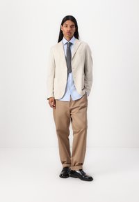 Light beige blazer with a textured fabric, paired with a light blue shirt and beige trousers. Black shoes complete the outfit.