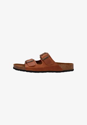 Brown leather slide sandal with two adjustable buckles, cork footbed, and black rubber sole, side view.