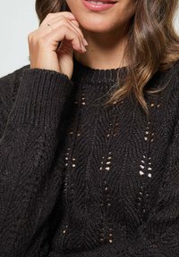 Pull en maille noire avec un motif texturé et un design à mailles ouvertes. Comprend un col et des poignets côtelés.