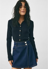 Námornícky rebrovaný top s dlhým rukávom a zapínaním na gombíky, skombinovaný s tmavými džínsovými sukňami s vysokým pásom a striebornými gombíkovými akcentami.