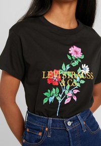 Czarny bawełniany T-shirt z wielokolorowym haftem kwiatowym oraz napisem "LEVI STRAUSS & CO" w żółtej literze. Krótkie rękawy, okrągły dekolt.