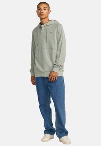 Lichtgroene geribbelde hoodie met trekkoorden, een knoopsluiting, en een voorzak, gecombineerd met blauwe straight-leg jeans en witte sneakers.