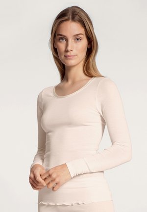 Camicia a maniche lunghe color crema con collo rotondo, realizzata in tessuto morbido. Presenta un design aderente e una texture liscia, con una leggera rigatura e un orlo ondulato.
