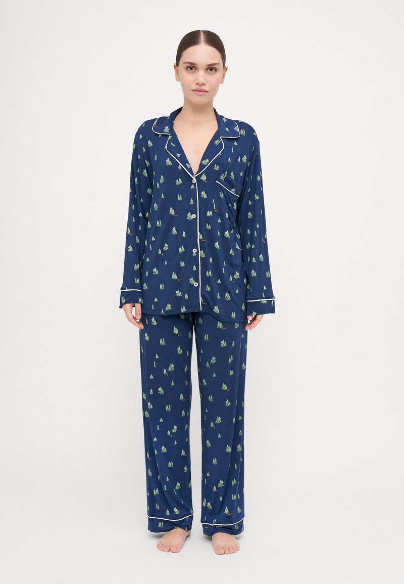 Navy blue pajama set in lightweight fabric, featuring a pattern of green trees and small accents, with white piping along the collar and cuffs.