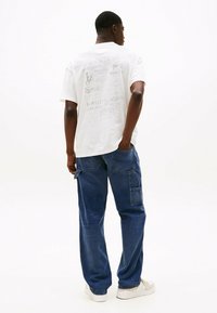 Camiseta blanca de algodón con un patrón gráfico en gris en la parte posterior; combinada con pantalones cargo de mezclilla azul con múltiples bolsillos.