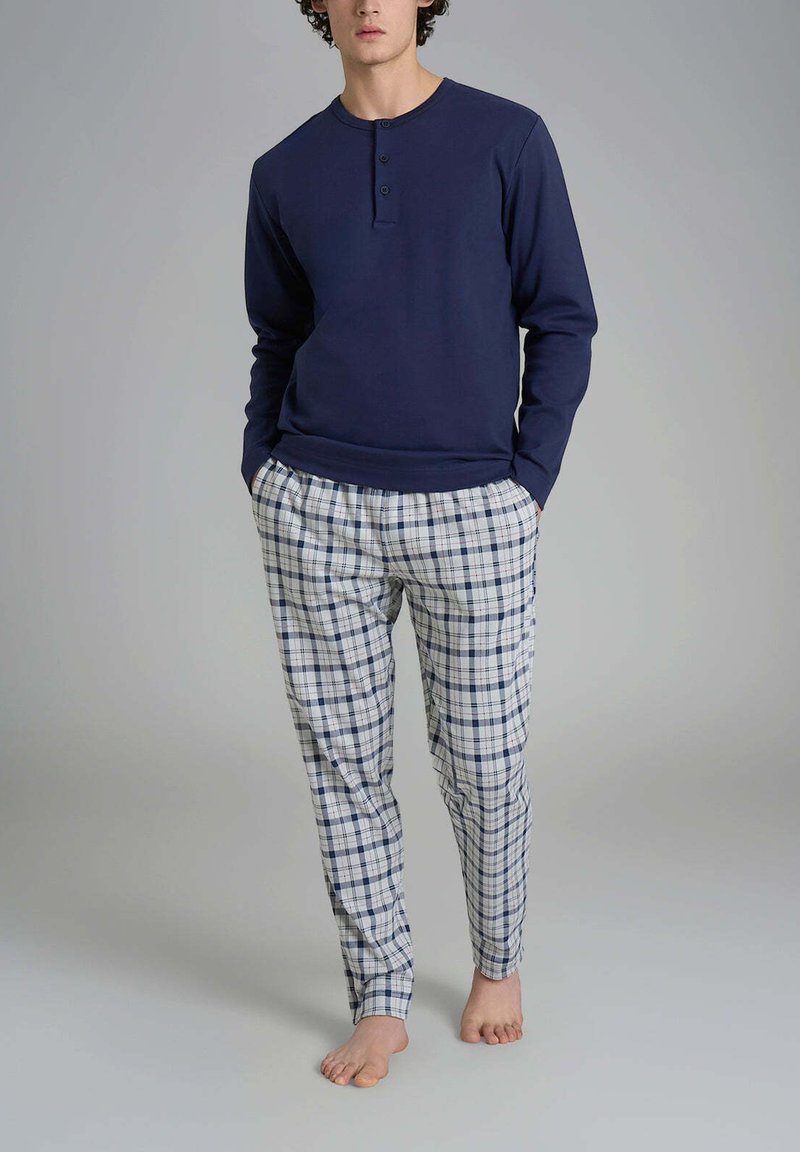 Maglia a maniche lunghe blu navy con collo a giro e tre bottoni, abbinata a pantaloni a quadri bianchi, blu navy e azzurri.