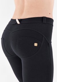 Leggings neri con un design retroilluminato nella parte posteriore, texture liscia e dettagli in hardware dorato; include un particolare tasca curva unica.