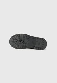 Soletta di scarpa in gomma nera con pattern di grip texture, dotata di fori di ventilazione circolari e dettagli di branding sottili.