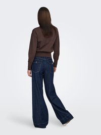 Bruine trui en donkerblauwe wijde denim spijkerbroek. De spijkerbroek heeft een klassiek ontwerp met vijf zakken, een licht verweerde afwerking en opgerolde pijpen.