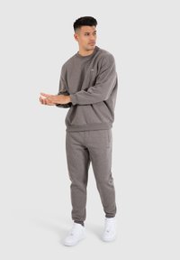 Sweatshirt gris et joggers assortis en tissu doux ; présente un col rond et un détail de logo discret ; associé à des baskets blanches.