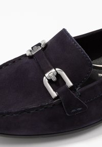 Navy-Suede-Schuh mit Metallverschlussakzent, genähten Details und abgerundetem Zehenbereich. Glatte Textur und flexible Sohle. Nahaufnahme.