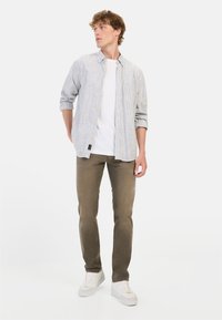 Lichtgrijs gestreept overhemd met knopen, witte t-shirt eronder, olijfgroene slim-fit broek en witte sneakers. Casual outfit voor mannen.
