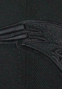 Schwarze Stoffmütze mit gestickten Details, strukturiertem Oberflächenmaterial und abgerundeten Steppnähten. Das Material wirkt robust und stabil.