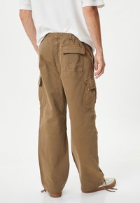 Koffiekleurige cargo broek met een relaxte pasvorm, voorzien van meerdere zakken, een elastische tailleband en verstelbare boorden. Gemaakt van een duurzame stof.