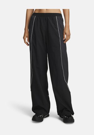 Black wide-leg pants with white side piping worn by a person standing, paired with black athletic shoes.