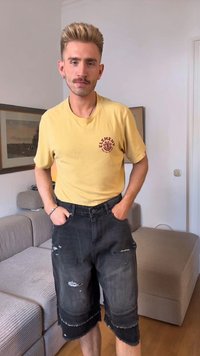 T-shirt amarela com um logo gráfico vermelho, combinada com calções de denim pretos desgastados com bordas desfiadas e um corte largo.