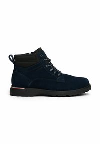 Bottines en suede bleu marine avec col rembourré noir, bout rond, lacets à l'avant, semelle noire et petit détail de rayure rouge, blanche et bleue.