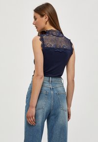 Dunkelblaues ärmelloses Top mit Spitzenverzierungen am Rücken, kombiniert mit hellblauen, weiten Jeans mit einem ausgewaschenen Finish und zwei Gesäßtaschen.