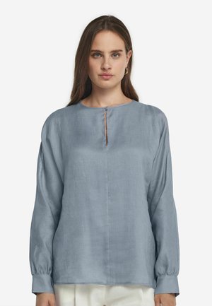 Hellblaue Bluse mit langen Ärmeln aus einem strukturierten Stoff, mit einem runden Ausschnitt und einer kleinen Öffnung sowie schmalen Bündchen.