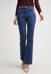 Mörkblå utsvängda jeans i denim, med klassisk femfickdesign, metallknapp och sydda sömmar.