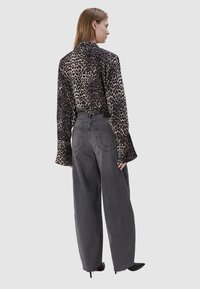 Blouse met luipaardprint met lange, uitlopende mouwen en grijze broek met wijde pijpen. De blouse heeft een gladde textuur; de broek heeft opvallende achterzakken.