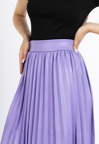 Plisseret lilla nederdel med en glat, blank talje. Stoffet har en blød tekstur og et flydende design, der fremhæver bevægelse og drapering.