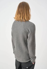 Grauer Strickpullover mit strukturiertem, geripptem Design. Hat lange Ärmel und einen runden Ausschnitt, mit einem leicht abgerundeten Saum am unteren Ende.