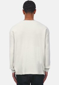 Camisa blanca de manga larga con costura acanalada, de corte relajado y cuello redondo, que presenta hombros caídos y tejido texturizado. La vista trasera muestra un diseño minimalista.